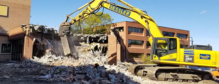 Yellow Excavator Demolishing Brick Building, Operated by Demolition Contractors